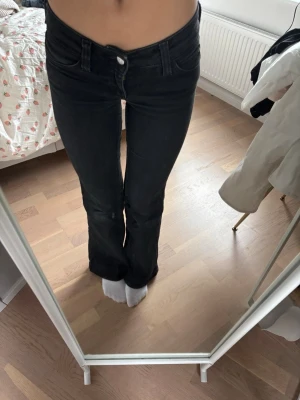 Svarta bootcut jeans - Säljer ett par svarta bootcut jeans med klassisk femficksdesign och normalhög midja. Jeansen har en lätt utsvängd passform nedtill och stängs med knapp och dragkedja. Perfekta till sneakers eller boots för en trendig look.