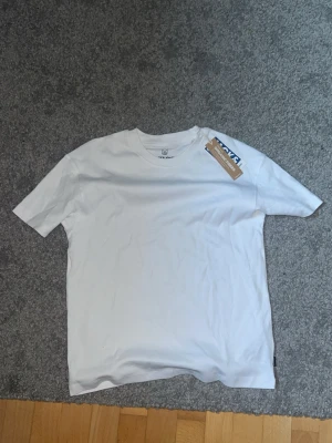 Vit basic t-shirt från Jack & jones - Klassisk vit t-shirt från Jack & Jones  med rund hals och korta ärmar. Tillverkad i mjuk bomull för en skön känsla och enkel stil. Perfekt att matcha med jeans eller shorts för en clean look.