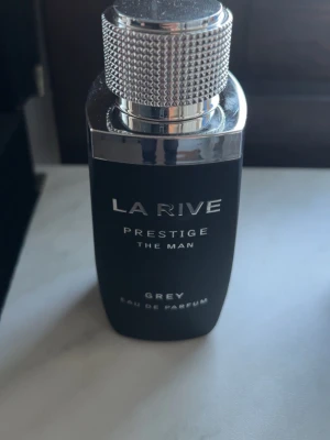 La Rive Prestige The Man Grey EdP - La Rive Prestige The Man Grey Eau de Parfum är en stilren herrparfym i en matt svart flaska med silverfärgad metallkork och detaljer. Flaskan har en modern, maskulin design och rymmer en elegant doft för dig som gillar exklusiva parfymer. 100ml