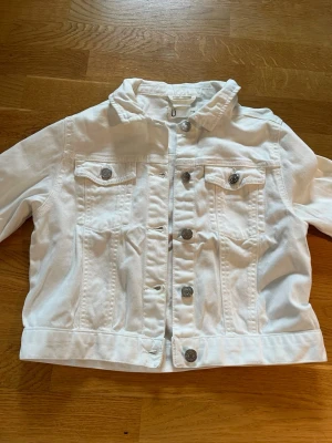 Vit jeansjacka från Kappahl - Snygg vit jeansjacka från Kappahl i storlek 146, men motsvarar typ XXS, måttet uppifrån och ner är 39 cm. Den är i bra skick använd några gånger och har en liten fläck under den mittersta knappen, men inget som syns tydligt. Hör av er om frågor och kontakta mig innan köp!💗(Säljer även på Vinted ifall man skulle vilja köpa där)