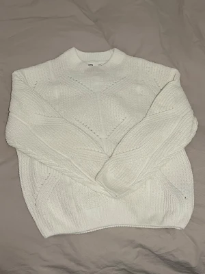 Vit stickad tröja  - Säljer en vit stickad tröja med snyggt strukturmönster och rund halsringning. Tröjan har långa ärmar och ribbade muddar vid ärmslut och nederkant.