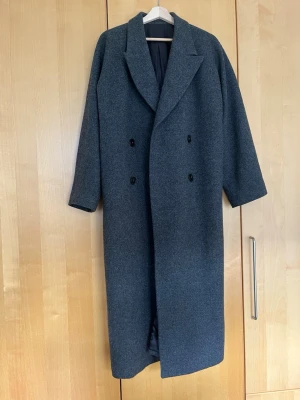 Grå ullkappa från Lis Bonne (tillverkas ej längre) - Grå oversized kappa i 100% ull i storlek 36 från Lis Bonne Atelier. Litet hål i högra fickans söm i innefodret som enkelt går att laga. Tillverkas ej längre! Perfekt vårjacka / vårkappa. Hämtas på Södermalm i Stockholm, eller postas mot frakt.