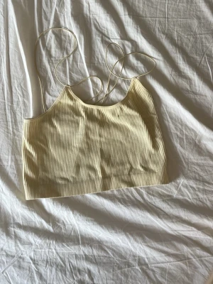 Ljus ribbad linnetopp med smala band - Säljer en ljusgul ribbad topp med smala axelband. Toppen har en croppad passform och är perfekt för varma dagar. Materialet är mjukt och stretchigt, vilket gör den superbekväm att bära.