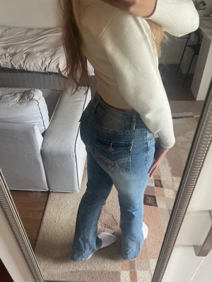 Blå bootcut jeans med broderad ficka - Mid/Låg-midjade bootcut jeans i blåtvätt. Med fina broderidetaljer och knapp på bakfickan som får rumpan poppa superfint. 