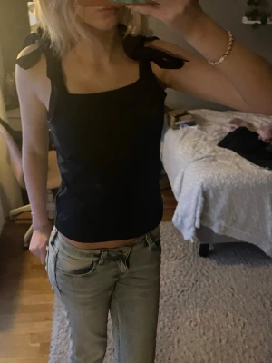 Mörkblå  linnetopp med knytaxlar - Säljer en mörkblå linnetopp med breda axelband som knyts i stora rosetter. Toppen har en rak, croppad passform och fyrkantig ringning. Perfekt att styla med jeans eller kjol för en trendig look.