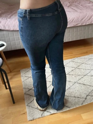 Lågmidjade jeans utan bakfickor - Säljer ett par blå bootcut jeans med låg midja och utan bakfickor. Jeansen har en snygg tvätt och är tillverkade i stretchigt denimtyg som sitter bekvämt. Perfekta för dig som gillar en retroinspirerad look. 