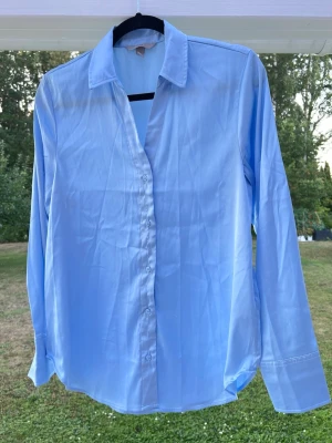 Ljusblå satinskjorta från H&M, stl S - En ljusblå skjorta i satin från H&M. Köptes ett par år tillbaka men blev dessvärre aldrig använd 🩵 Passar bra för sig själv eller som overshirt över en topp exempelvis! Längd: 68 cm - Axel: 40 cm