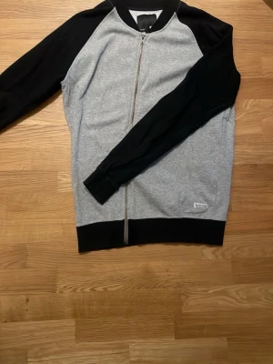 Grå och svart zip hoodie - Snygg hoodie från Weekday i grått med svarta ärmar och muddar. Dragkedja framtill och klassisk rak passform. Perfekt för en avslappnad streetwear-look. Tillverkad i mjuk bomullsblandning för extra komfort.