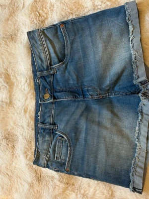 Blå jeansshorts från LAB Industries - Snygga blå jeansshorts från LAB Industries med rå kant nertill och klassisk femficksdesign. Shortsen har knapp- och dragkedjestängning samt en avslappnad passform. Perfekta för varma dagar och enkel att matcha med olika toppar.