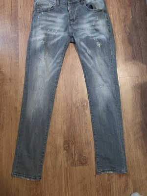 Grå slitna jeans från Dsquared2 - Säljer ett par grå jeans från Dsquared2 med slitningar och tvättade detaljer. Modellen är smal med klassisk femficksdesign och patch bak med texten 'Eviction Notice'. Perfekta för dig som gillar streetwear och en avslappnad look.