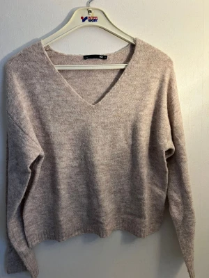 Beige stickad tröja från 157 - Mysig beige stickad tröja från 157 med v-ringning och långa ärmar. Tröjan har en mjuk och fluffig känsla, perfekt för kalla dagar. Enkel design som passar till det mesta och ger en avslappnad look.