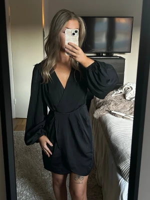 Svart omlottklänning med puffärm - Snygg svart miniklänning med omlott från NA-KD. Aldrig använd, endast testad. Storlek 34. Säljs för 150kr. Skriv om det önskas fler bilder på klänningen. 💛