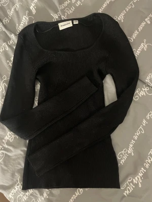 Svart glittrig ribbstickad tröja Kappahl - Snygg svart ribbstickad tröja från Kappahl med lång ärm och bred, rundad urringning. Tröjan är figurnära och har en enkel, stilren design som passar till det mesta. Perfekt basplagg för din garderob. 