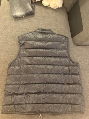 Svart dunväst från Moncler - Snygg svart dunväst från Moncler med quiltad design och två dragkedjeförsedda fickor framtill. Västen har hög krage och Moncler-logga på bröstet. Perfekt för lager-på-lager och streetwear-vibe.