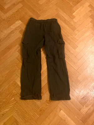 Mörkgröna cargobyxor med fickor - Säljer ett par mörkbruna cargobyxor med raka ben och stora sidofickor. Byxorna har resår i midjan för extra komfort och är tillverkade i ett mjukt tyg som känns skönt mot huden. Perfekta för en avslappnad och trendig stil.Skriv gärna för mått! 💕