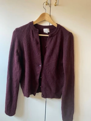 Vinröd kofta - Mysig vinröd kofta med rund halsringning och knappar framtill. Långärmad modell i mjukt stickat material, perfekt att slänga över en t-shirt eller topp. Ribbstickade muddar vid ärmslut och nederkant för extra komfort. missar en knapp men det är en extra på lappen som ses på sista bilden, lätt o sy på!!