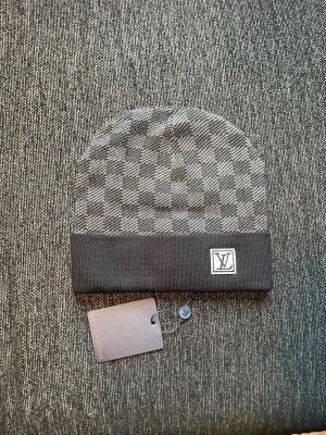 Zara  - Snygg grå mössa från Zara med klassiskt rutmönster och svart uppvikt kant. På kanten ger en exklusiv touch. Perfekt accessoar för dig som gillar stilrena detaljer och designerplagg.