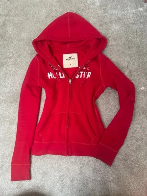 Röd zip hoodie från Hollister - Snygg röd hoodie från Hollister. M men sitter som S. Fint skick! Kolla in mina andra annonser.🥰