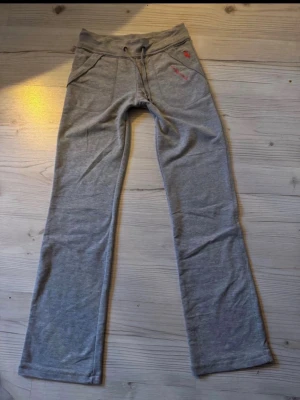 Grå mjukisbyxor från Abercrombie & Fitch  - Grå mjukisbyxor från Abercrombie & Fitch med lätt Bootcut  och dragsko i midjan. Byxorna har två fickor fram och detaljer med rosa broderi, inklusive en älg och loggan. Tillverkade i mjukt bomullsmaterial som är skönt att ha på sig. Dock mer S än M i storlek 