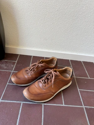 Bruna lädersneakers med vit sula - Bruna sneakers i läder med lågt skaft och vita sulor. Skorna har bruna skosnören, diskreta sömmar och en klassisk, stilren design. Perfekt för dig som gillar en enkel och tidlös look.