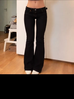 Svarta bootcut jeans med låg midja - Säljer ett par svarta bootcut jeans med låg midja. Jeansen har utsvängda ben och sitter tight upptill för en snygg siluett. 