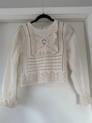 Vit virkad blus med spetsdetaljer - Supersöt vit blus med virkade partier och spetsdetaljer framtill. Blusen är långärmad och har puffärmar med smock vid ärmslut och rund halsringning. Materialet är tunt och luftigt, perfekt för en varm sommardag. Knäppning bak i nacken. Säljer då den inte används. Har använt den 1 gång. Nypris 399kr, men säljs inte längre! 