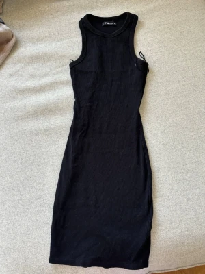 Svart ribbad klänning från FB Sister - En svart, ribbad klänning från FB Sister i storlek S. Klänningen är ärmlös, har en kroppsnära passform och är av kortare modell. Perfekt för dig som gillar en enkel men stilren look.