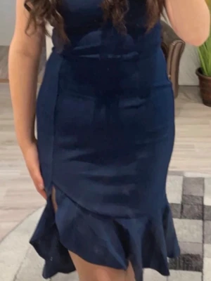 Marinblå volangklänning med slits - Snygg marinblå klänning med volangdetaljer och slits framtill. Klänningen har en figurnära passform och är tillverkad i ett mjukt, följsamt material. Perfekt för dig som vill ha en elegant look med lite extra attityd.