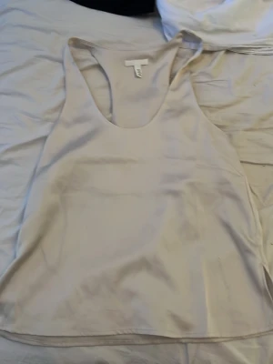 Beige linnetopp från H&M - Säljer en enkel och stilren beige linnetopp från H&M. Toppen är ärmlös med rundad halsringning och har en mjuk, slät yta som ger en skön känsla. Perfekt att matcha med jeans eller kjol för en clean look.