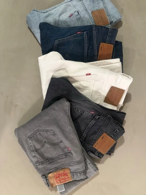 Levi's jeans i olika färger 5st - Säljer flera par klassiska Levi's jeans i olika färger: ljusblå, mörkblå, vit, svart och grå. Alla har den ikoniska röda Levi's-lappen och läderpatch bak. Perfekta raka ben och tidlös design som funkar till allt. W29-28 L32.