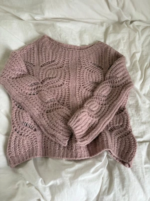 Rosa stickad tröja med mönster - Säljer en rosa stickad tröja med snyggt hålmönster och långa ärmar. Tröjan har rund halsringning och är gjord i ett mjukt garn som känns fluffigt. Perfekt för att bli varm men inte svettig. 