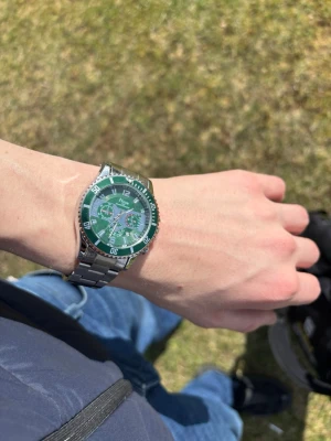 Grön klocka från Fossil med stållänk - Snygg klocka från Fossil med grön urtavla och silvrig stållänk. Klockan har tydliga siffror, datumvisning och flera små urtavlor för extra funktioner. Klassisk rund form och sportig look som sticker ut på handleden. Pris kan diskuteras bid snabb affär! Har dock tappat en sak på den!!!