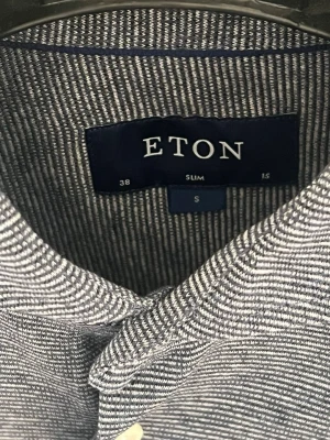 Slim fit skjorta från Eton - Säljer en knappt använd slim fit skjorta från Eton med diskret randigt mönster och klassisk krage. Skjortan har vita knappar och lång ärm, perfekt för dig som gillar stilrena plagg med snygg passform.