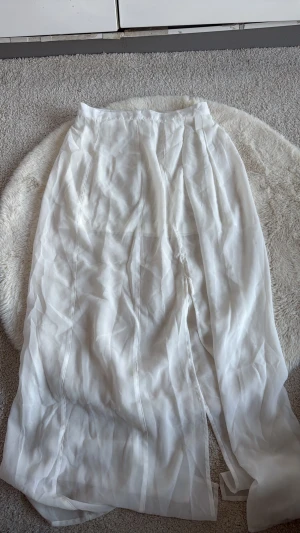 Vit långkjol från Jeans & Clothes - Säljer en elegant vit långkjol från Jeans & Clothes i storlek XS. Kjolen är gjord i ett tunt och lätt material som ger ett flowigt och luftigt intryck. Perfekt för dig som gillar stilrena och klassiska plagg med enkel design.