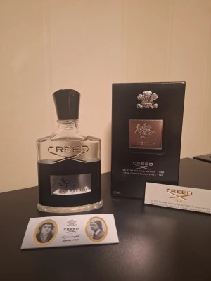 Creed Aventus Eau de Parfum - 100 ml - Creed Aventus Eau de Parfum i 100 ml flaska. Flaskan är genomskinlig med svart etikett och silverdetaljer, samt svart kork. Medföljer originalförpackning och certifikat. Lyxig och ikonisk doft som passar dig som vill sticka ut.                               ⚡️ Snabba svar på meddelanden 💬 Tveka inte att skicka ett meddelande om du har frågor. 📦 Snabb frakt – skickar samma eller nästa dag efter beställning.  🏷Lägg flera varor i bundle för upp till 20% rabatt. 