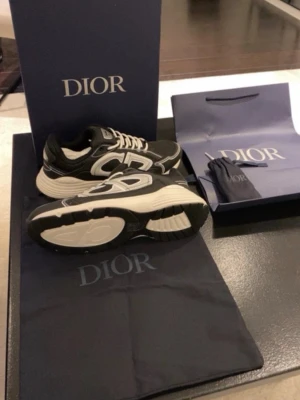 Svarta B30 - Snygga svarta b30 sneakers med vita och grå detaljer samt stora CD-loggor på sidorna. Skorna har vita snören och en tjock, vit sula med svart mönster undertill. Tillverkade i en mix av mesh och läder för en modern look.