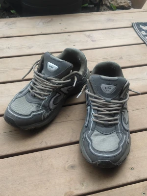 Sneakers - Säljer ett par sneakers med coola detaljer i både mesh och läder. Skorna har en chunky design, gråa snören och logotyp på plösen. Perfekt för dig som vill ha en trendig och exklusiv look. Snygga kontraster mellan olika grå nyanser och material.