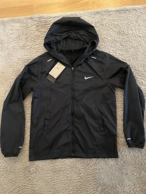 Nike Stride Repel - Svart Nike Stride Repel jacka/vindjacka ny skick i storlek S, men passar även S/XS i vissa fall. Perfekt för våren och sommaren. Den har väl fungerande reflex, och kommer samt med dustbag och tags. Mått finns. Prisförslag & frågor är välkomna! 🙏💬