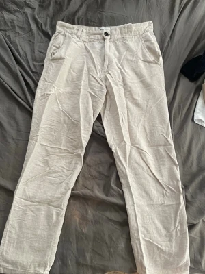 Beiga linnebyxor med raka ben - Säljer ett par stilrena beiga linnebyxor med raka ben och klassisk knappstängning. Byxorna har två sidofickor och är tillverkade i ett lätt och luftigt linnematerial som passar perfekt för en avslappnad look. Jack n Jones