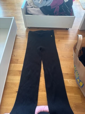 Svarta ribbade leggings från Aim'n - Säljer ett par svarta ribbade leggings från Aim'n med hög midja och utsvängda ben. Leggingsen har en liten guldfärgad metallbricka med ananaslogga vid midjan. Stretchigt och mjukt material som sitter snyggt och bekvämt.