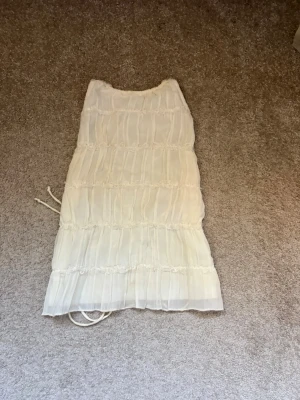 Vit omlott topp med snörning - Säljer en vit omlott topp med snörning i sidorna och volangdetaljer. Toppen är ärmlös och har ett lätt, luftigt tyg som ger en romantisk känsla. Perfekt att styla med jeans eller kjol för en trendig look.