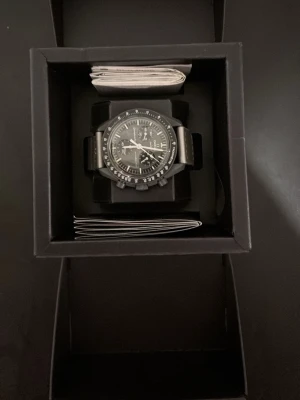 Omega x Swatch Mission to Mercury - Snygg svart Omega x Swatch Speedmaster Mission to Mercury klocka med sportig design. Klockan har svart urtavla, svarta detaljer och svart armband. Kommer i originalförpackning. Perfekt för dig som gillar stilrena accessoarer och ikonisk design. Klockan är använd mycket sällan 3-4 gånger max