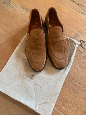Brunello Cucinelli Loafers i Ljusbrun Mocka/Suede, Storlek 44 - Ett par eleganta loafers från Brunello Cucinelli. Skorna är endast provade och aldrig använda, vilket tydligt framgår av insidan och sulorna. En idealisk modell för en sofistikerad och ledig stil. Kartong och skopåse medföljer. Skoblock ingår inte.