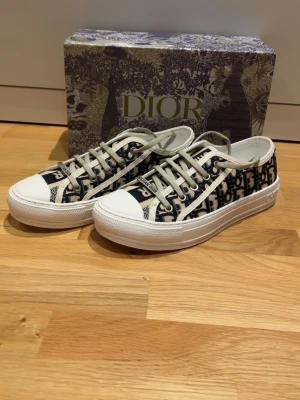 Dior låga sneakers - Säljer ett par dam Dior sneakers med klassiskt blått och vitt mönster. Skorna har vita gummisulor, vita snören och med Dior-logga. Perfekt för dig som vill ha en exklusiv och trendig look.