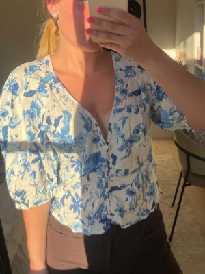 Blommig blåvit blus med knappar🩵 - Söt blus med blått blommönster på vit botten. Modellen har v-ringning, puffiga trekvartsärmar och knäppning framtill. Luftigt material, perfekt för varma dagar. Ger en fräsch och somrig vibe till din outfit.