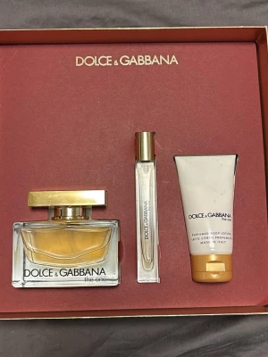 Dolce & Gabbana The One parfymset - Lyxigt parfymset från Dolce & Gabbana The One med en elegant glasflaska parfym, en smidig reseflaska och en matchande body lotion. Flaskan har guldfärgat lock och detaljer, och lotionen kommer i en vit tub med guldfärgad kork. Reseflaskan har används lite men annars är allt oöppnat, som nytt. Perfekt present till dig själv eller någon du gillar.