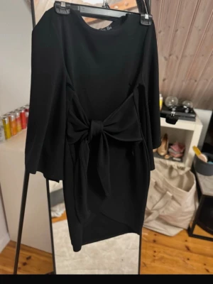 Svart klänning med knut  - En svart klänning från boohoo med långa ärmar och en stor knytrosett framtill. Klänningen har en enkel, elegant design med rund hals. Perfekt för dig som gillar stilrena detaljer.
