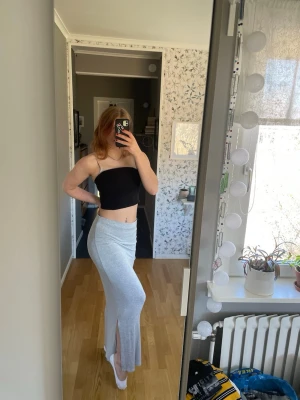 Ljusgrå långkjol med slits - Säljer en ljusgrå långkjol i mjukt material. Kjolen har en rak passform och en snygg slits på sidan som ger extra rörelsefrihet. 