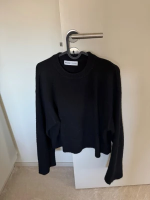 Svart stickad tröja från Bershka - En svart stickad tröja från Bershka med rund halsringning och långa ärmar. Tröjan har en enkel och stilren design, perfekt för lager-på-lager och passar till det mesta. Mjuk och skön att bära under kyliga dagar.