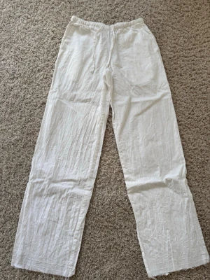 Vita linnebyxor med resårmidja - Snygga och luftiga lågmidjade vita linnebyxor med rak passform och resår i midjan. Perfekta för en avslappnad och stilren look. Tillverkade i ett lätt och svalt linnematerial som ger en skön känsla hela dagen.